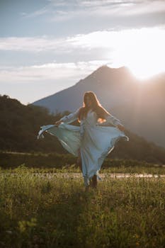 日落时分，一位穿着蓝色连衣裙的女人站在山间的草地上，拥抱大自然