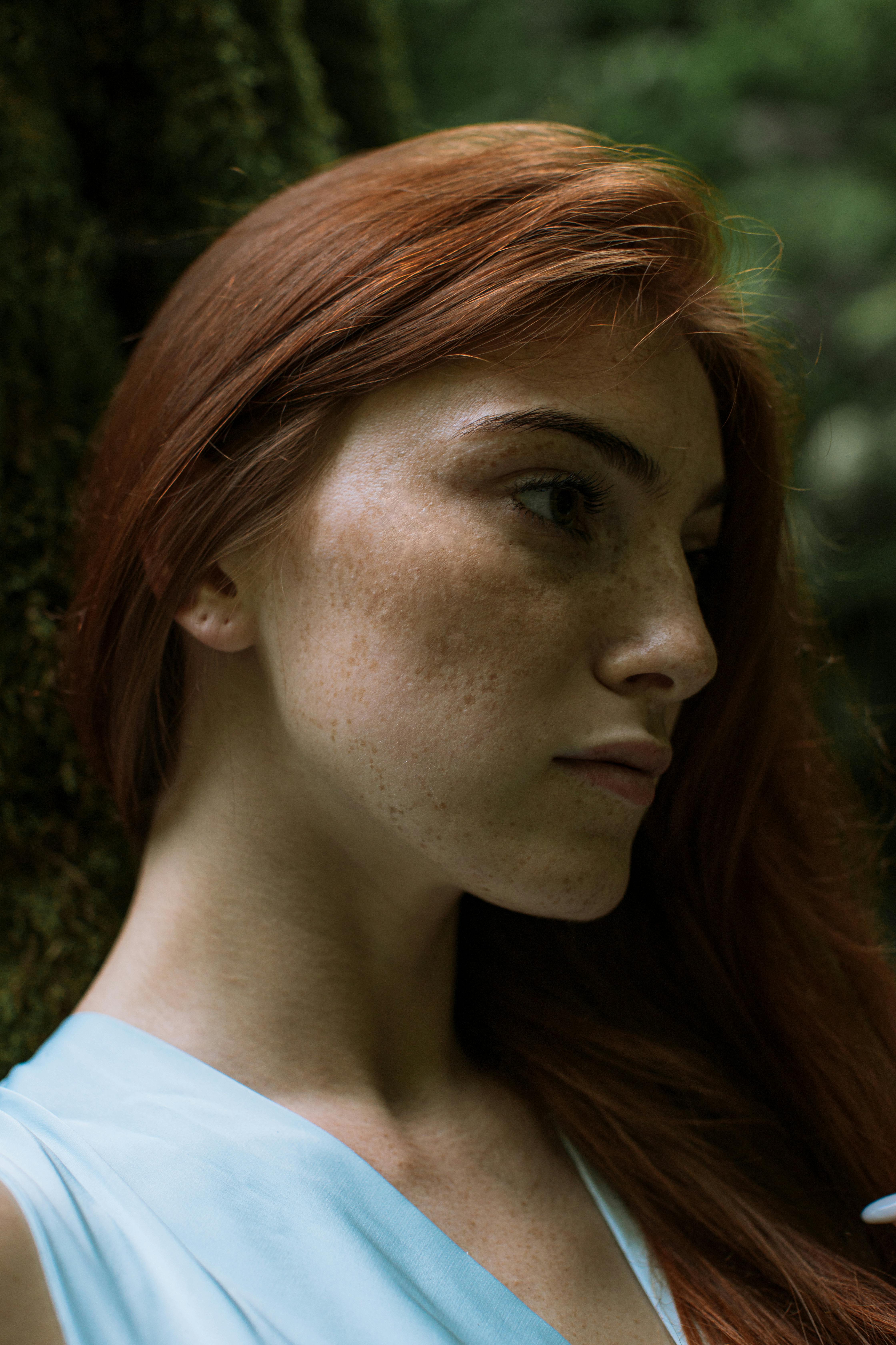 Close-up portrait of a young redheaded woman with freckles outdoors.