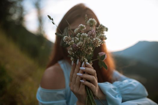 日落时分，一个修剪指甲的女人在风景秀丽的户外拿着野花