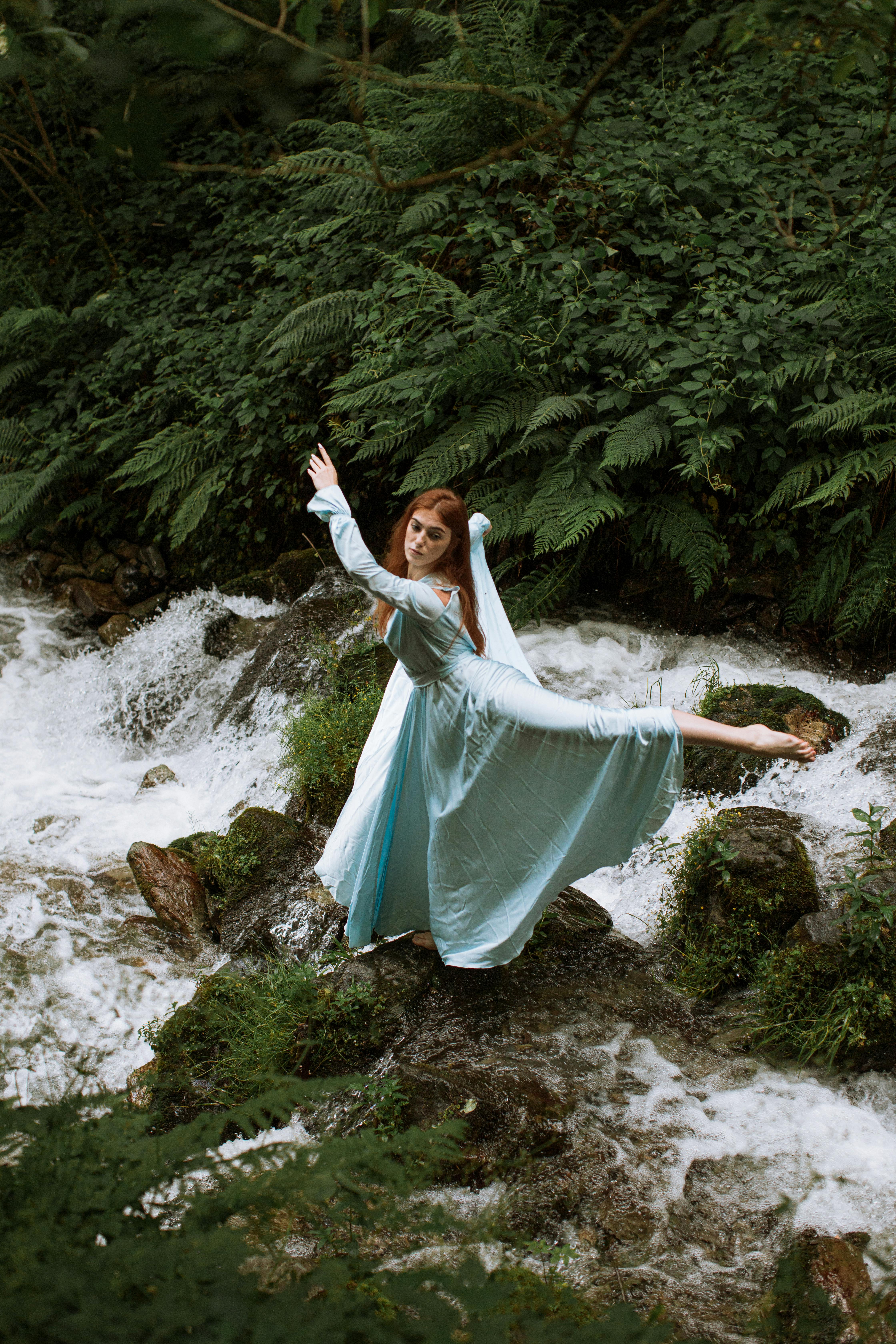 茂密的森林里，一个女人在溪边的岩石上优雅地跳舞