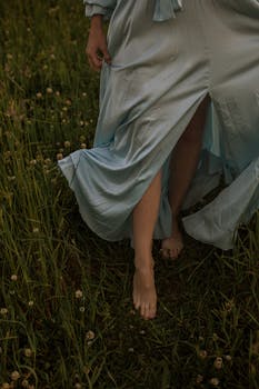 暮色中，一个穿着飘逸蓝色连衣裙的女人赤脚走过草地，捕捉到一个宁静的时刻