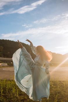 阳光明媚的日子里，一个女人穿着蓝色连衣裙，在户外山景前优雅地跳舞