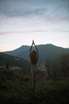 在多山的日出背景下，穿着连衣裙的女人表演树姿势，增添了宁静与力量
