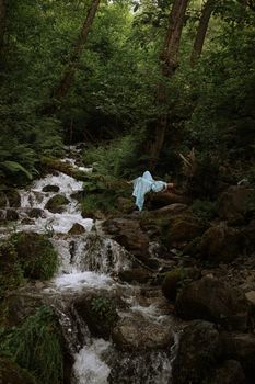 一个女人穿着白色连衣裙，躺在郁郁葱葱的森林里一条岩石河边