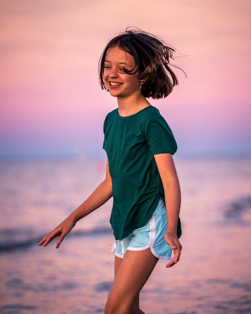Cheerful little girl wearing casual clothes with toothy smile and closed eyes standing in sea
