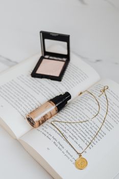Makeup and gold jewelry elegantly placed on a book on a marble surface.
