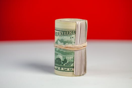 Rolled stack of US dollar bills secured with rubber band on bright surface contrast