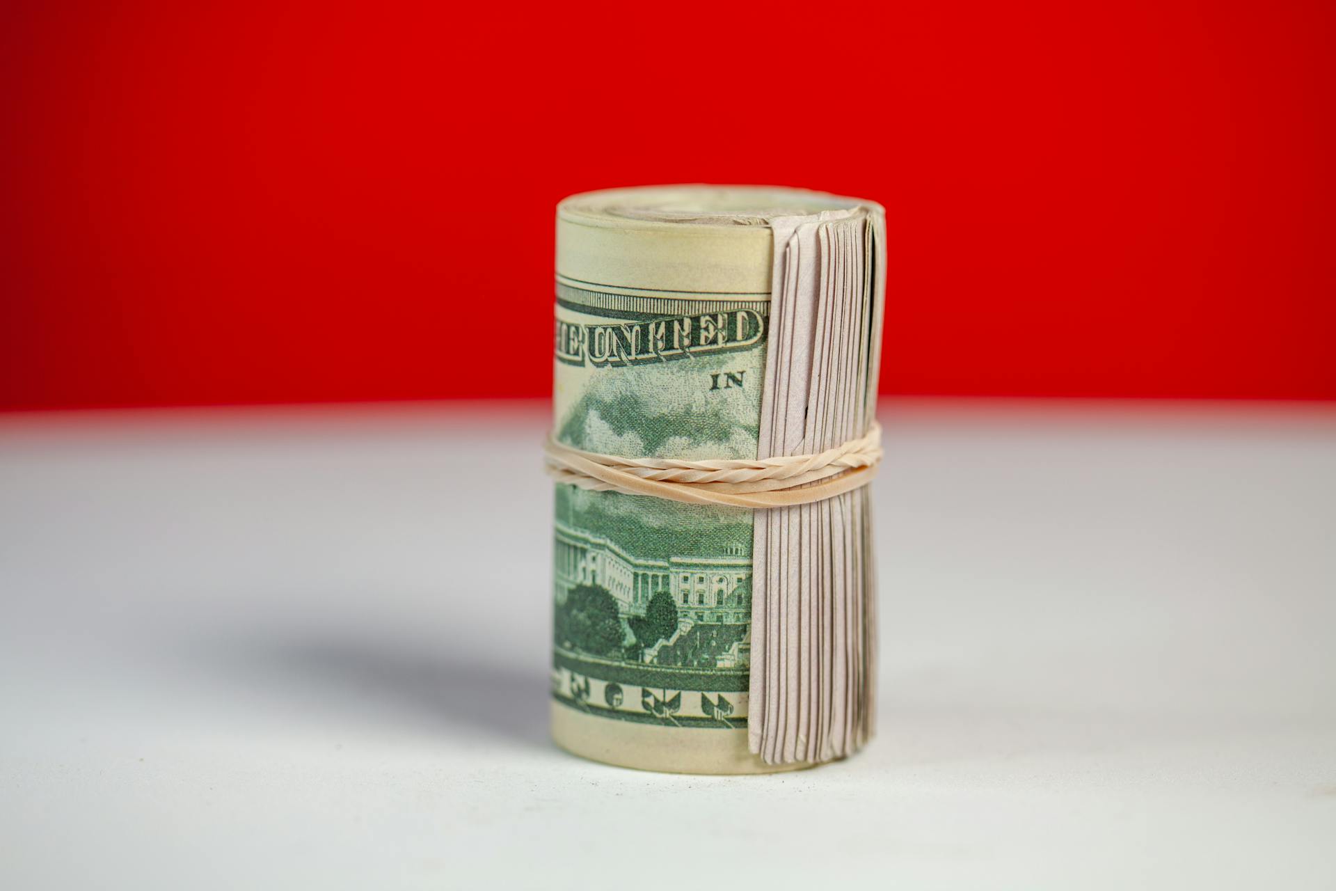 Rolled stack of US dollar bills secured with rubber band on bright surface contrast