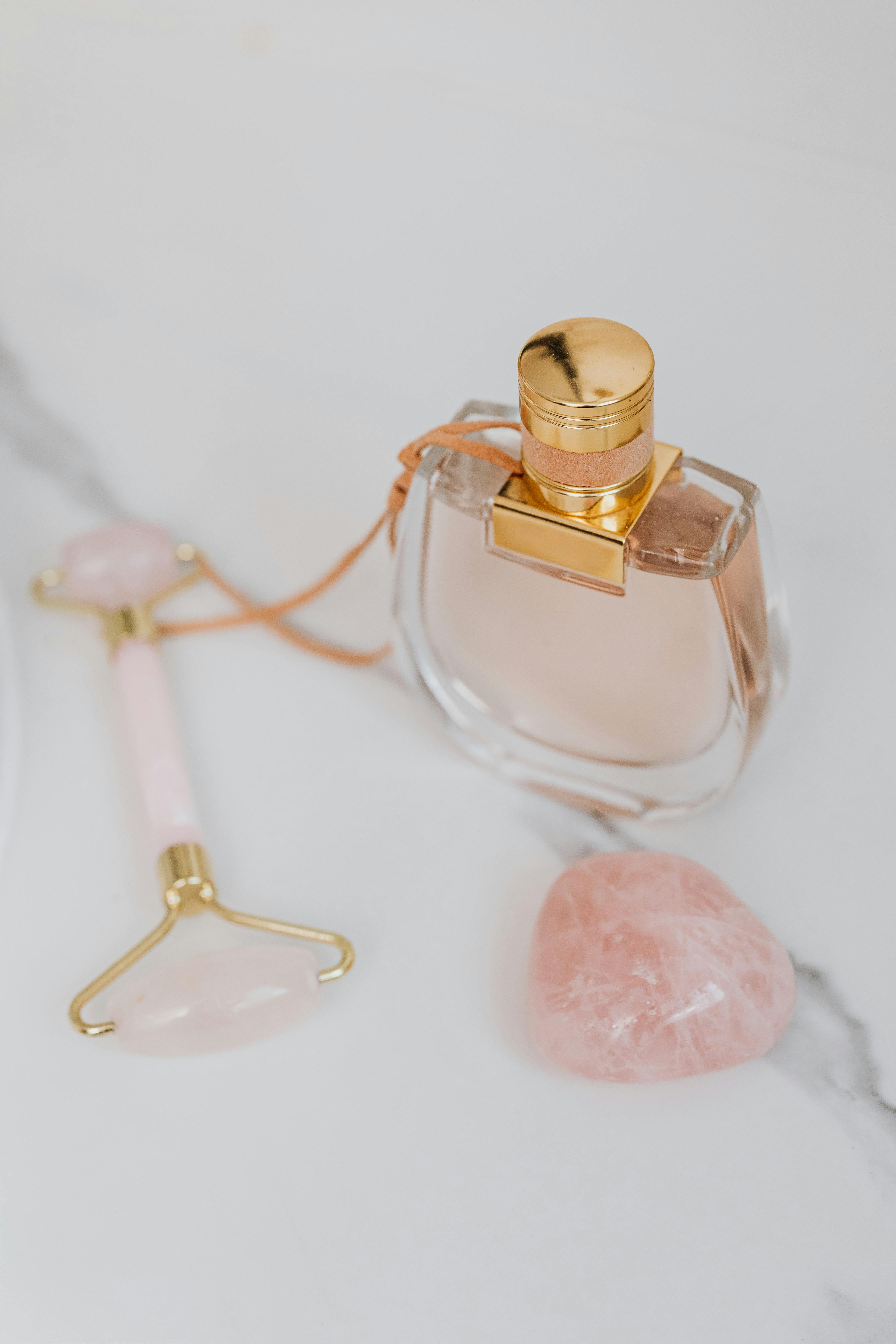 Close-up of a luxury perfume bottle with a jade roller and rose quartz on elegant marble.