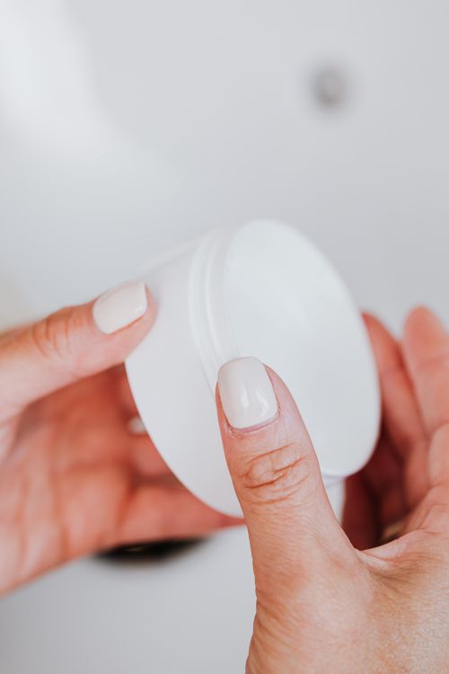 Free Close-up of a woman's manicured hands holding a white face cream jar against a blurred background. Stock Photo