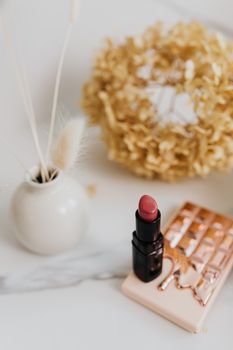 A sophisticated arrangement featuring red lipstick, a vase, and decorative items on a marble surface.