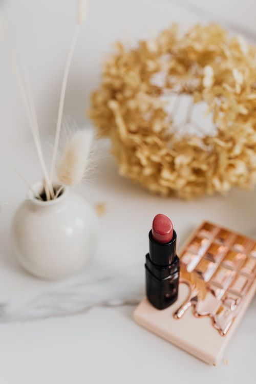 Free A sophisticated arrangement featuring red lipstick, a vase, and decorative items on a marble surface. Stock Photo