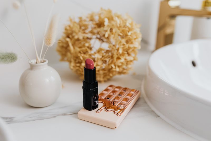 Red lipstick standing on a marble counter with natural decor, exuding elegance and minimalism.