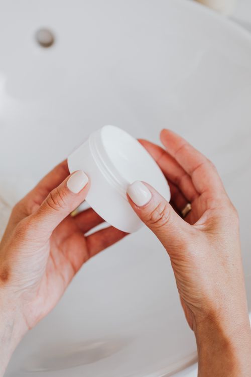Free Close-up of elegant hands holding a white cosmetic jar, ideal for beauty and skincare themes. Stock Photo