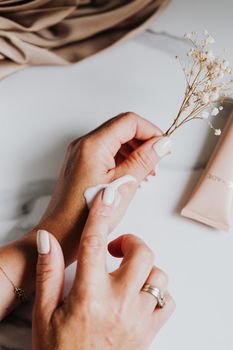 Close-up of manicured hands applying lotion with a delicate floral touch, perfect for skincare promotions.