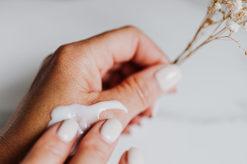 Close-up of hands applying cream with elegant nails and dried flowers