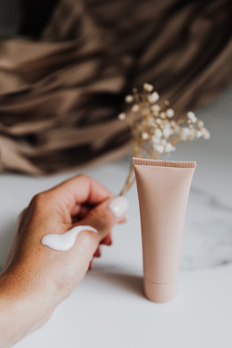 Person Holding Flowers Near Tube Hand Cream