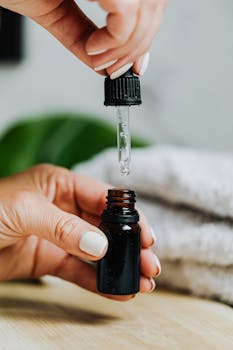 Close-up of a hand using a serum dropper over a skincare bottle on a wooden surface.