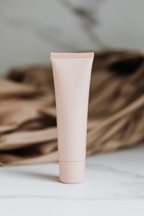 Free Elegant beige skincare bottle positioned on a marble surface with a soft textile backdrop. Stock Photo