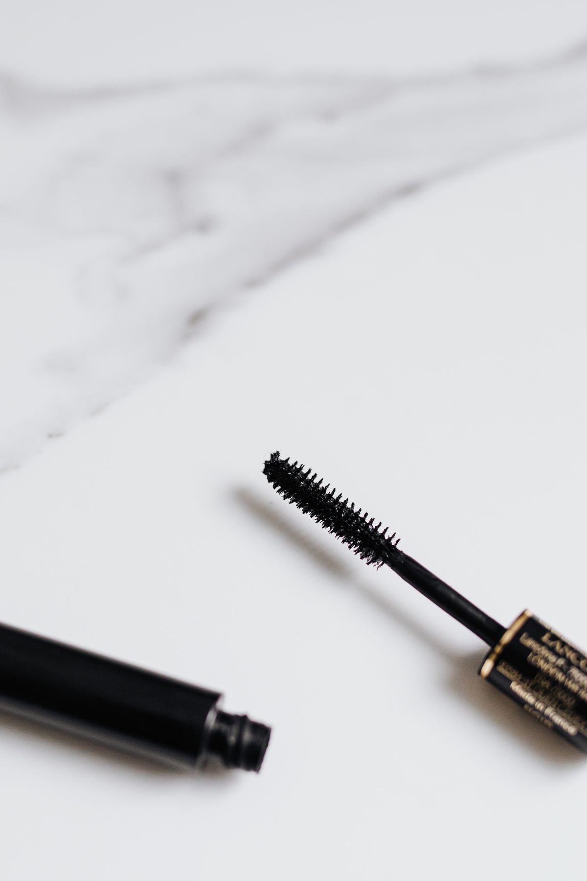Open mascara tube and wand resting on a pale marble surface