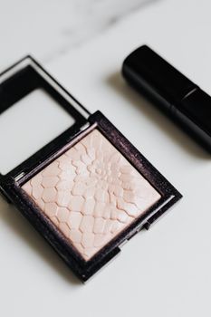 Flat lay of a textured highlighter compact and lipstick on a white surface, perfect for beauty and cosmetic themes.