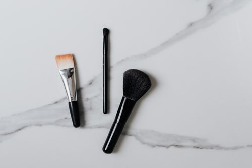 Free Flat lay of three different makeup brushes on a marble surface. Stock Photo