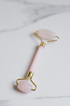 Elegant rose quartz facial roller for skincare on clean marble background.