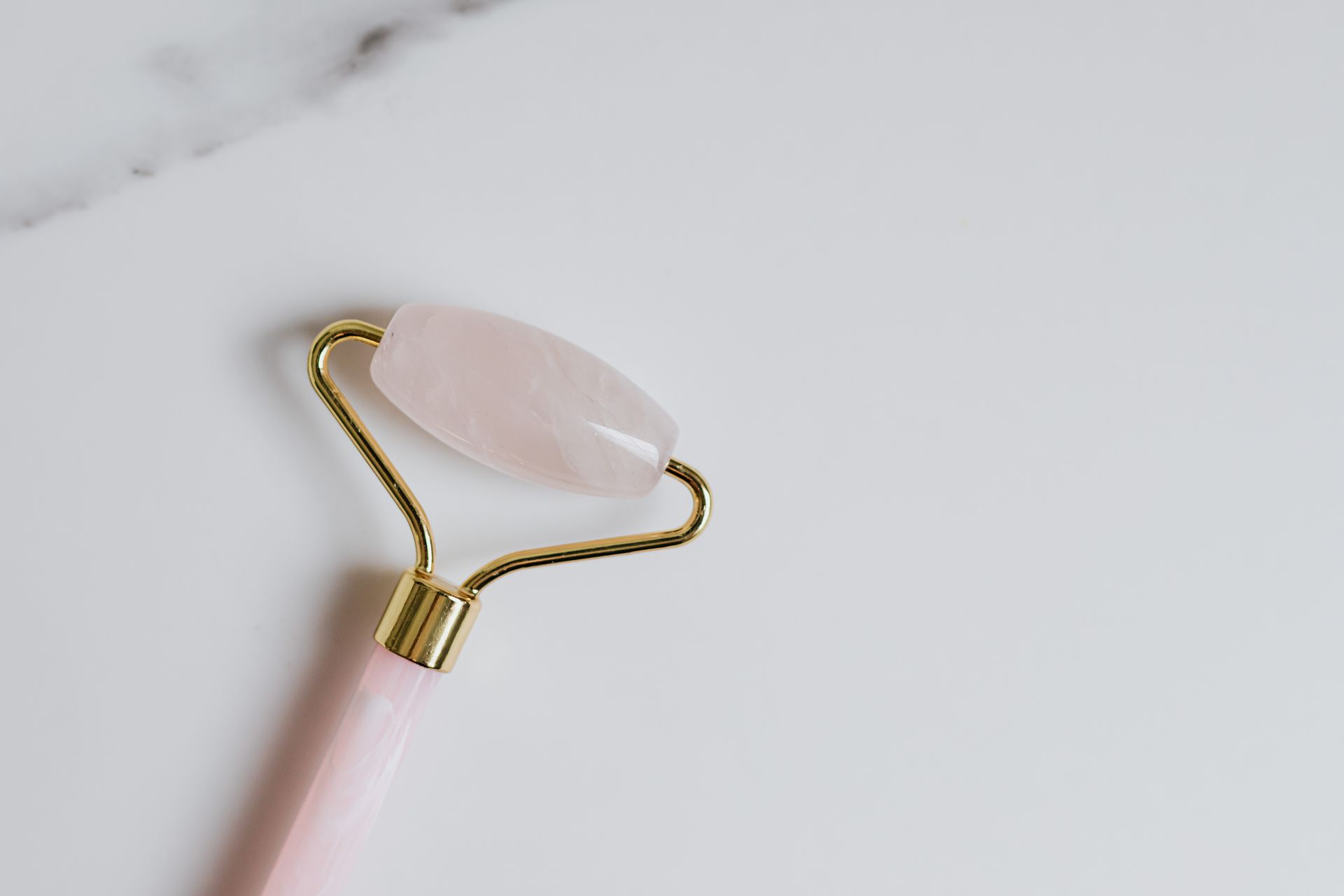 Close-up of a rose quartz facial roller on a smooth white surface, highlighting beauty and skincare.