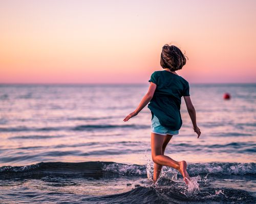 Free Back view of unrecognizable little girl with bare feet running in sea at sunset in summer vacation Stock Photo