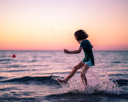 Free Side view of little girl playing with water in sea while having free time in summer evening Stock Photo