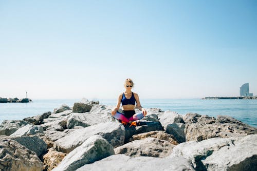 Free Woman Meditating on the Rocks by the Sea Stock Photo