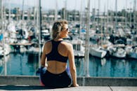 阳光明媚的日子里，一位穿着运动服的女人在码头欣赏着船只的景色，这是一种积极的生活方式