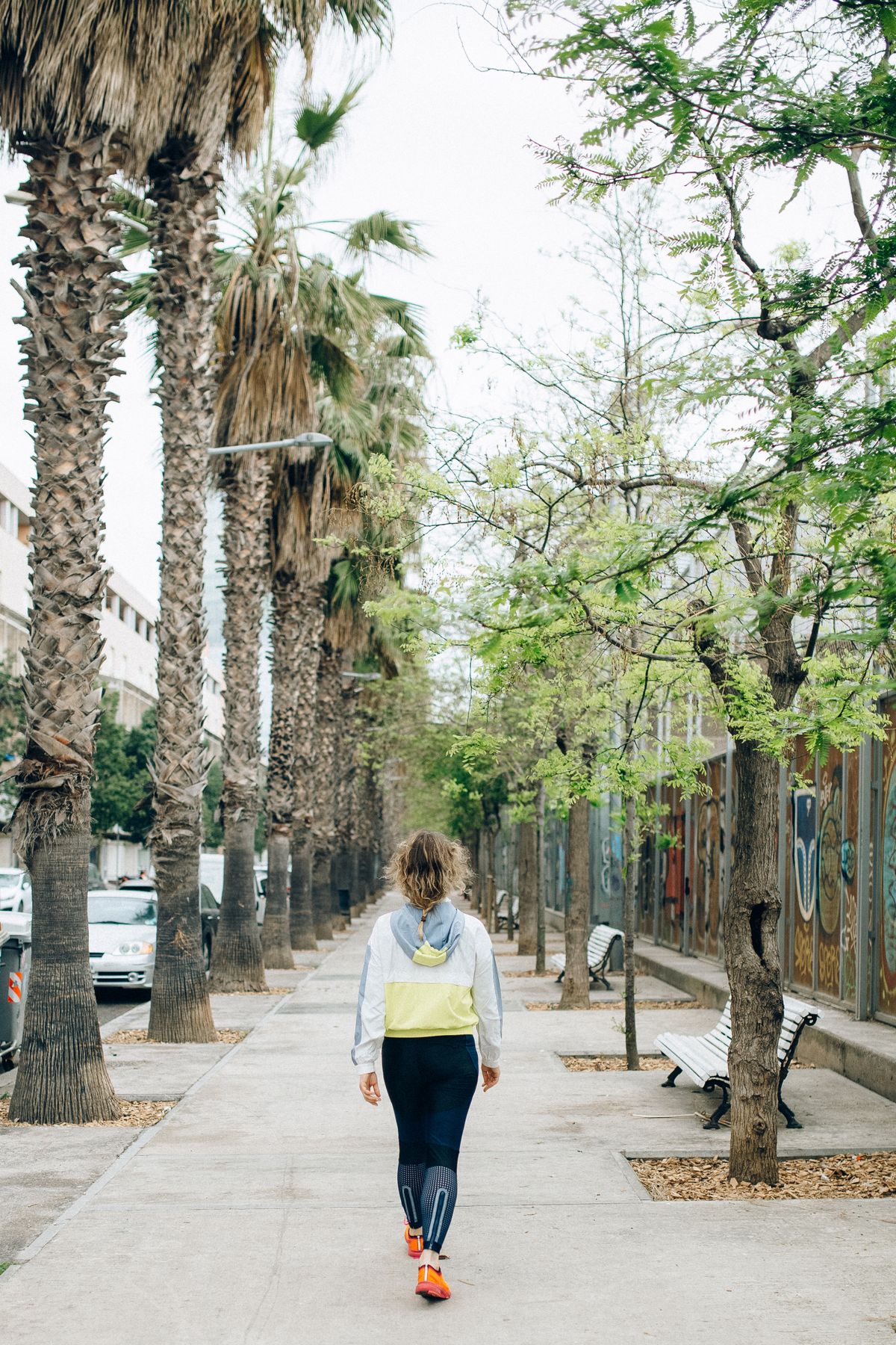 A woman in activewear walking outdoors along a tree-lined path in daylight.
