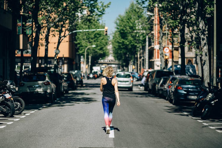 Back View Of A Woman In Activewear Walking In The Middle Of The Road