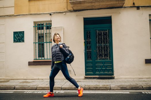 A smiling woman in activewear walks energetically on a sunny street, showcasing urban lifestyle.