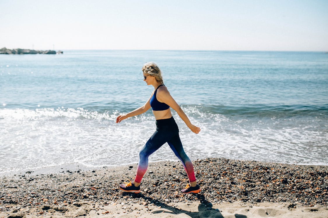 Free Woman in Black Tank Top and Blue Leggings Running on Beach Stock Photo