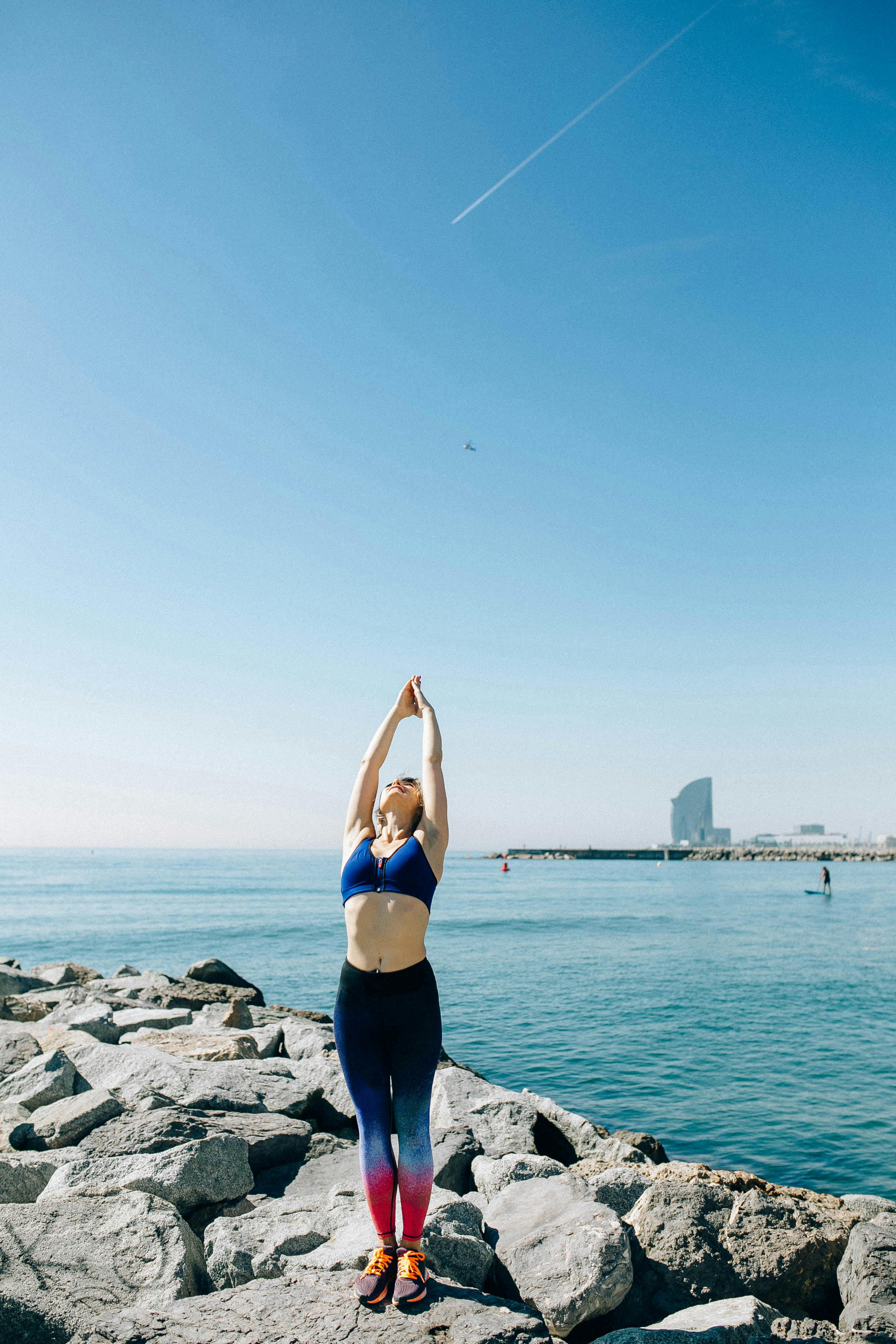 一名身穿运动服的妇女以海洋为背景，在岩石海岸线上伸展身体，展现了健康的生活方式