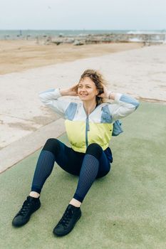 Smiling woman in activewear doing sit-ups on the beach, promoting a healthy lifestyle.