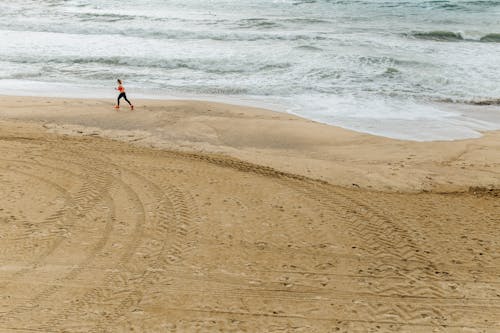 Photo of a Person Jogging on Brown Sand