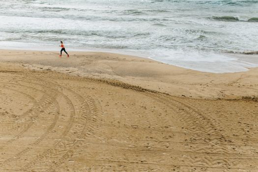 海浪拍打岸边，一个人沿着沙滩慢跑，营造出宁静的海岸锻炼场景