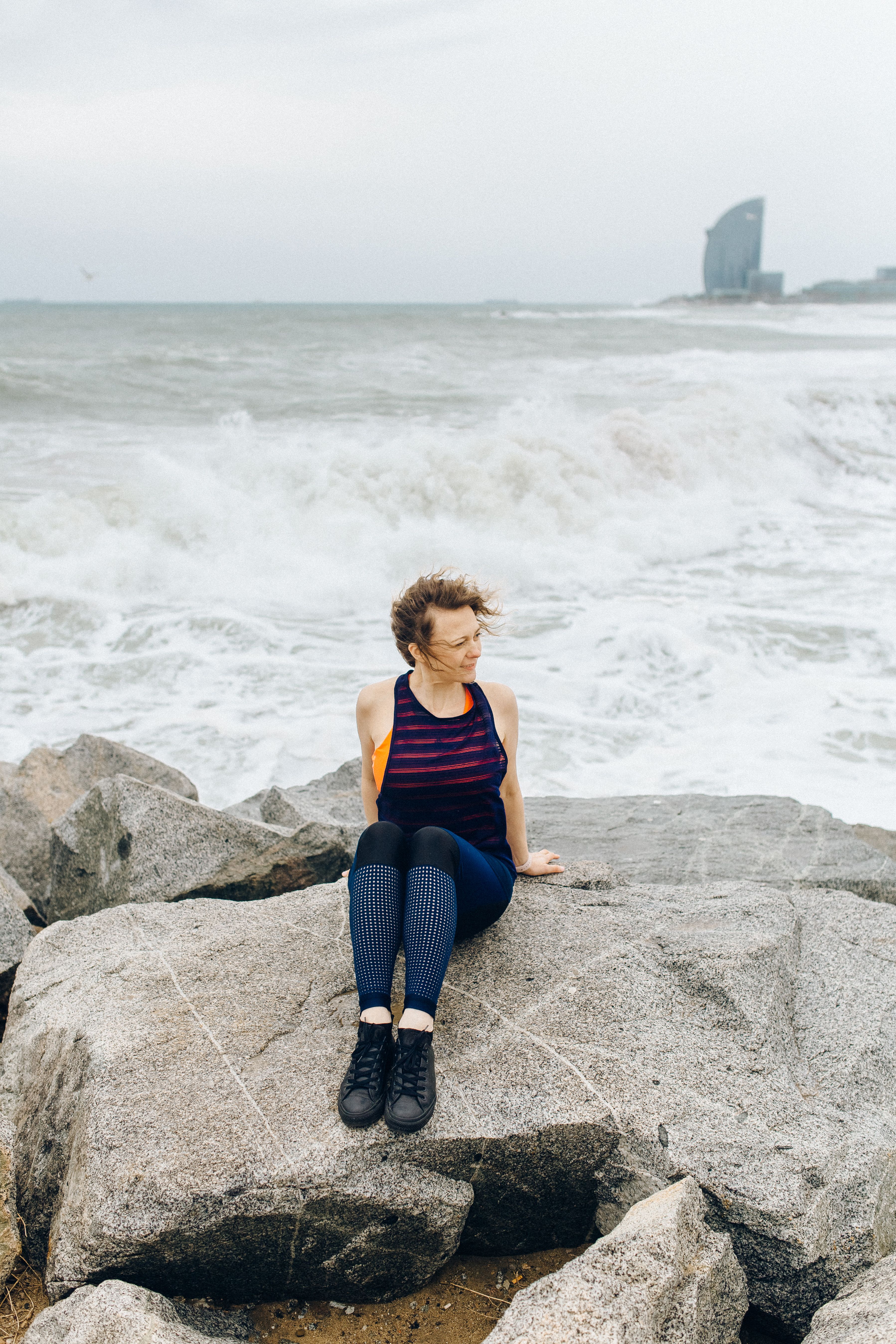 一名妇女坐在海边岩石上，背景是暴风雨中的海浪