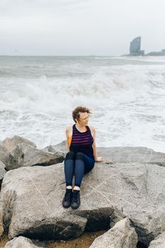 一名妇女坐在海边岩石上，背景是暴风雨中的海浪