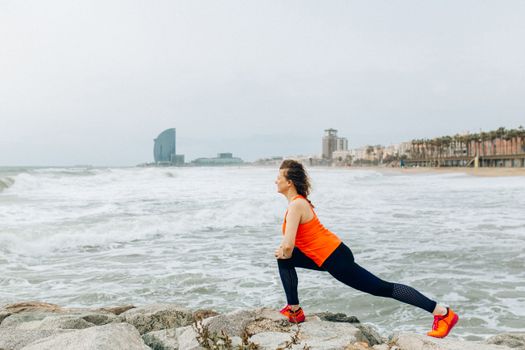 A woman stretches by the ocean in Barcelona, showcasing health and fitness by the sea.
