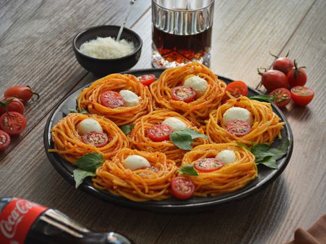From above of tasty spaghetti with cherry tomato slices and mozzarella near bowl with grated parmesan on wooden table
