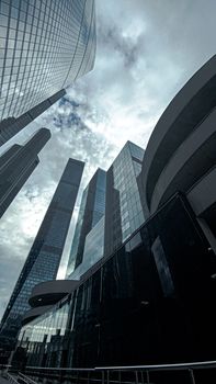 Low angle view of modern skyscrapers reflecting cloudy skies in a bustling urban cityscape.