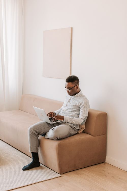 Free A man sits on a sofa, using a laptop in a minimalist home environment. Perfect shot for remote work themes. Stock Photo