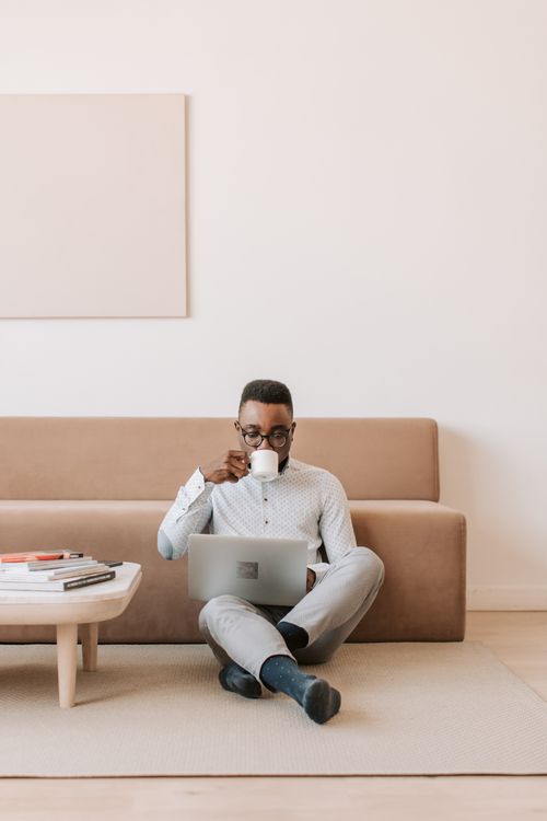 Free A man sits on the floor at home, drinking coffee and using a laptop. Stock Photo
