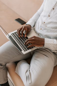 A man typing on a laptop while seated comfortably indoors, signifying remote work.