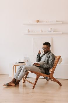 A man sips coffee while using a laptop at home, embodying remote work comfort.