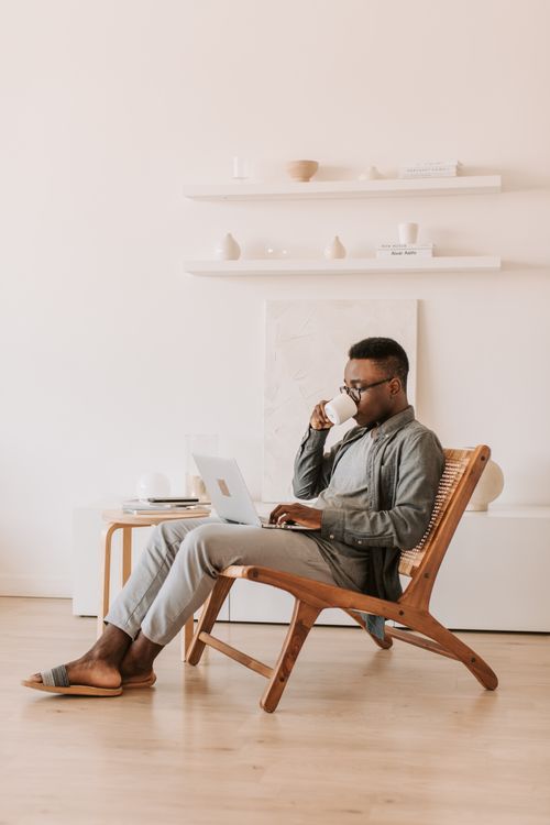 Free A man sips coffee while using a laptop at home, embodying remote work comfort. Stock Photo